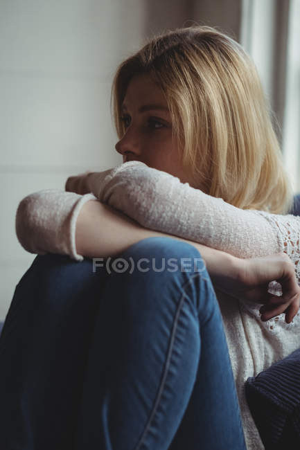 Thoughtful woman sitting on sofa in living room at home — Stock Photo