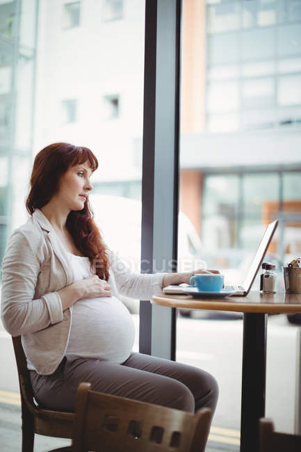 Femme d'affaires enceinte utilisant un ordinateur portable dans la cafétéria de bureau — Photo de stock