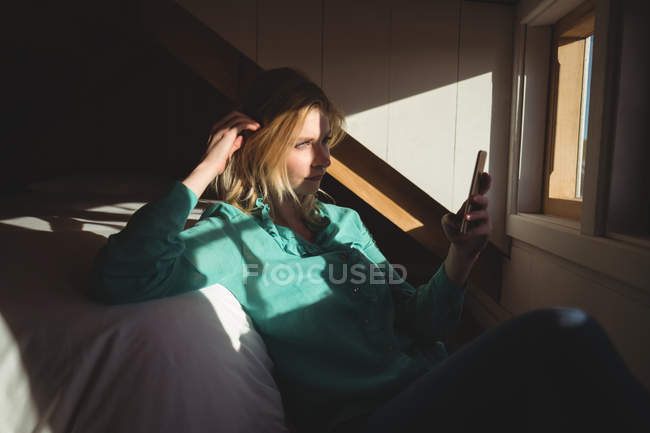 Beautiful woman using mobile phone in bedroom at home — Stock Photo