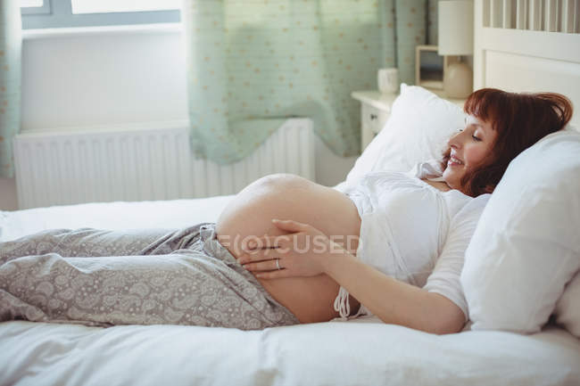 Беременная женщина отдыхает на кровати в спальне — стоковое фото