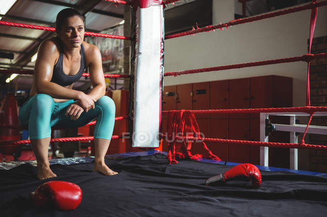 Задумчивая женщина-боксер сидит на веревке в боксерском ринге — стоковое фото