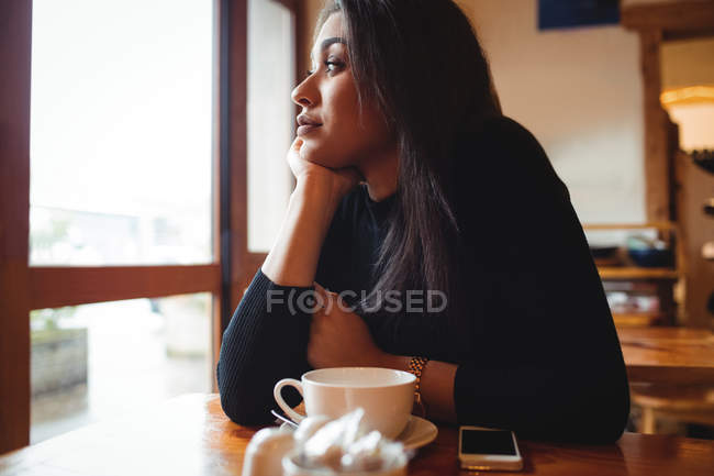 Mujer pensativa mirando a través de la ventana en la cafetería - foto de stock