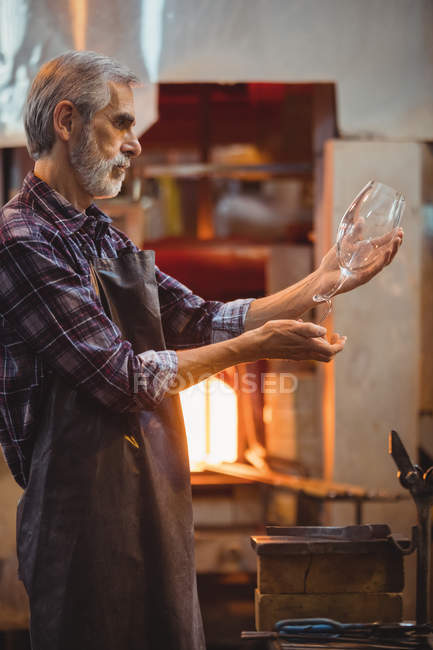 Стеклодув осматривает стеклоизделия на стекольном заводе — стоковое фото
