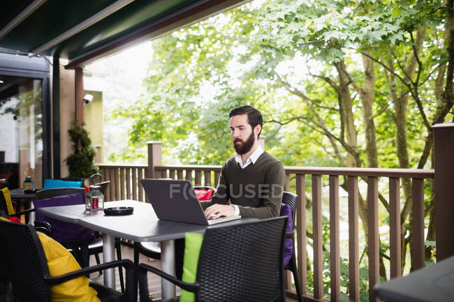Jovem usando laptop no terraço do bar — Fotografia de Stock
