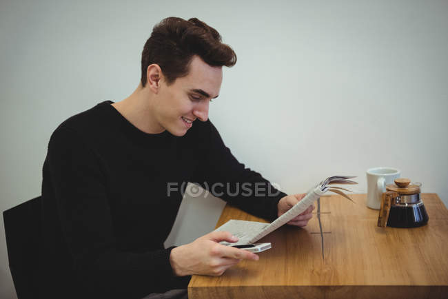 Man with mobile phone reading newspaper in coffee shop — Stock Photo