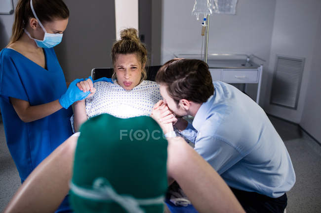 Doctor examining pregnant woman during delivery while man holding her hand in operating room — Stock Photo