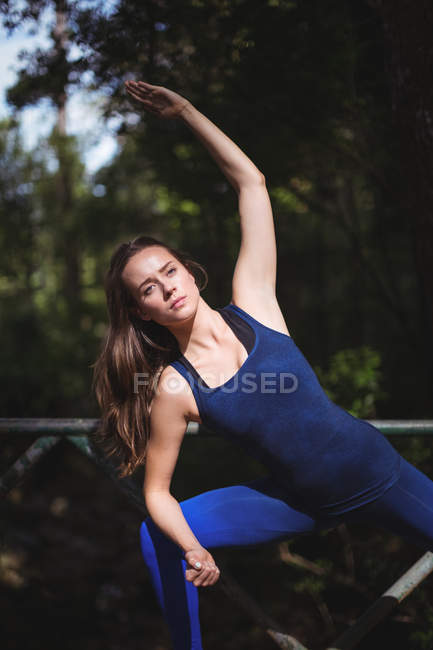 Woman doing stretching exercise on walkway bridge in forest — Stock Photo