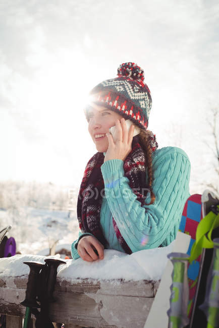 Smiling woman in winter wear talking on the phone against bright sunlight — Stock Photo