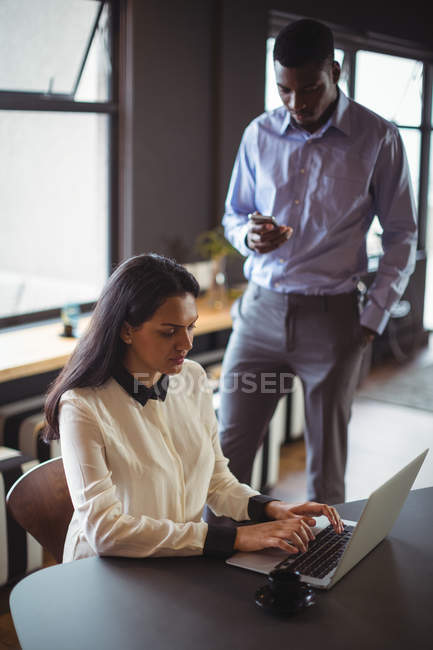 Businesswoman working on laptop while man using mobile phone in office — Stock Photo