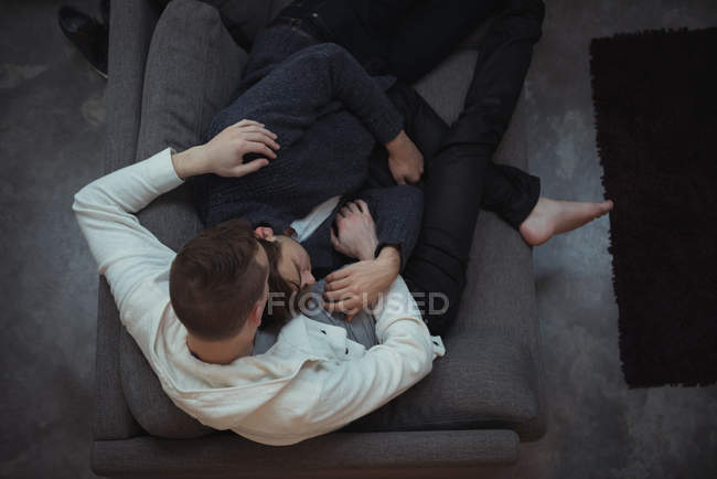 Gay casal abraçando enquanto relaxando no sofá no sala de estar — Fotografia de Stock