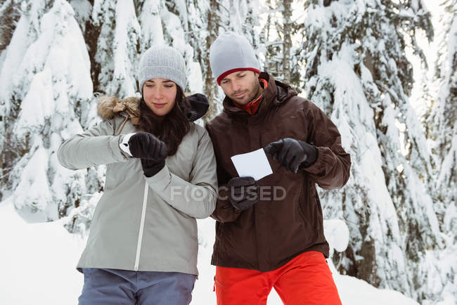 Woman checking her watch while man holding an address card on snowy landscape — Stock Photo