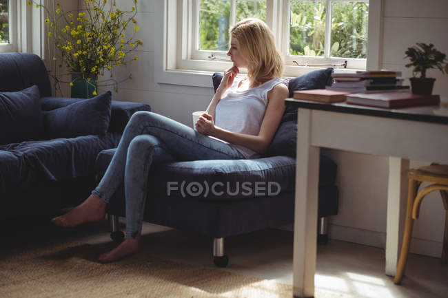Femme réfléchie prenant un café dans le salon à la maison — Photo de stock