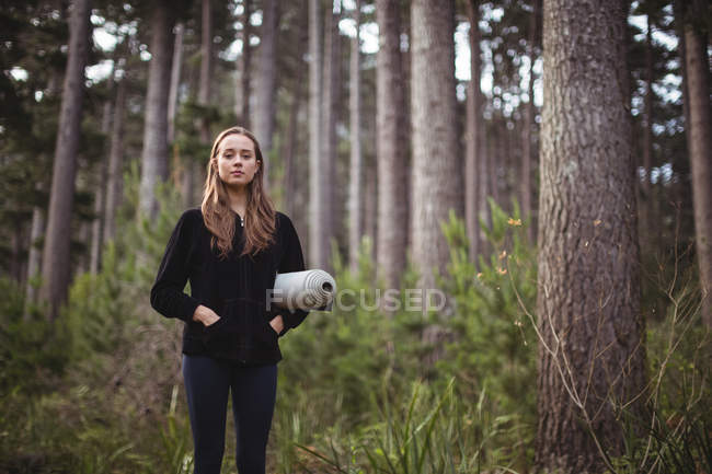 Ritratto di bella donna in piedi con tappetino da ginnastica nella foresta — Foto stock