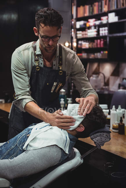 Barbeiro limpando o rosto do cliente com toalha quente na barbearia — Fotografia de Stock