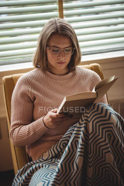 Femme assise sur une chaise et lisant un livre à la maison — Photo de stock