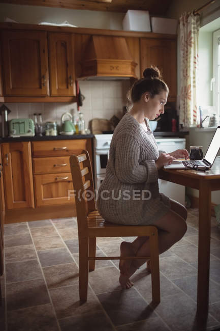 Mujer usando el ordenador portátil en la mesa en la cocina en casa - foto de stock