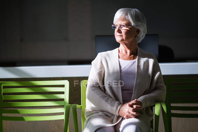 Mulher idosa pensativa sentada na cadeira no hospital — Fotografia de Stock