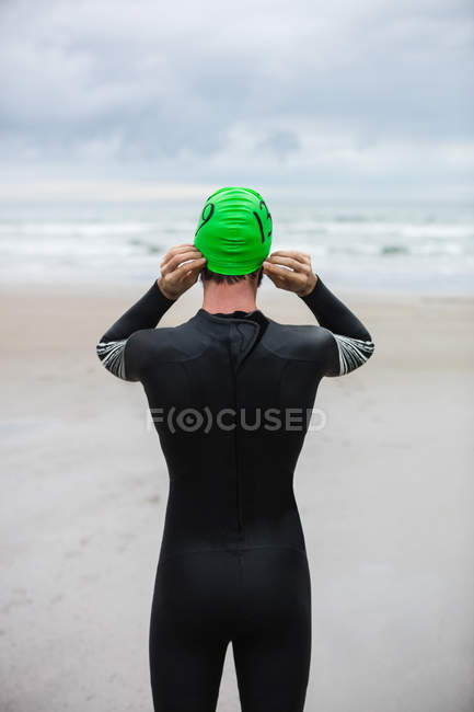 Vue arrière de l'athlète en combinaison de natation portant un bonnet de bain sur la plage — Photo de stock