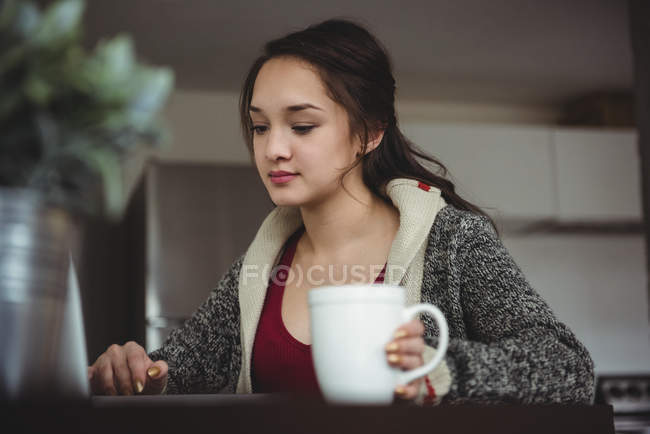 Жінка має каву під час роботи на ноутбуці вдома — стокове фото