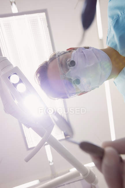 Vue à angle bas du dentiste tenant des outils dentaires à la clinique dentaire — Photo de stock
