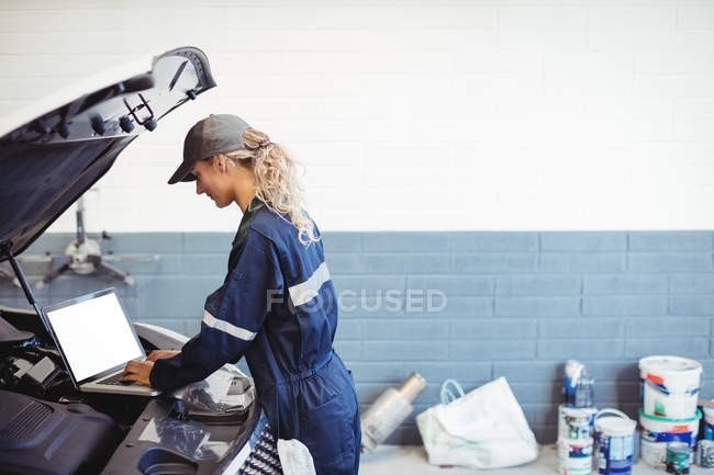 Mecánica femenina usando el ordenador portátil en el garaje de reparación - foto de stock