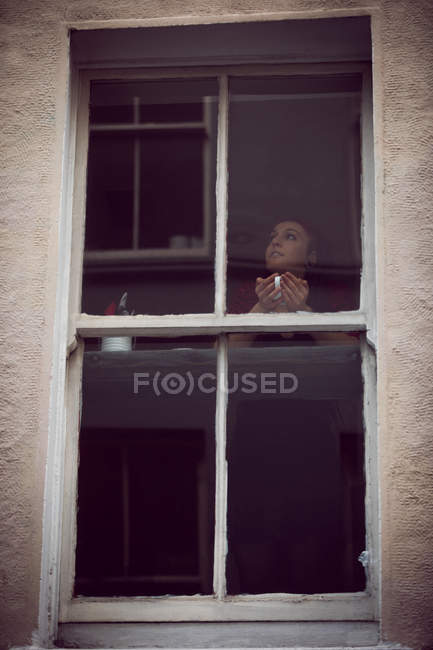 Femme regardant par la fenêtre tout en prenant un café dans le café — Photo de stock