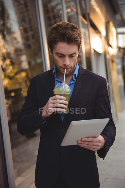 Homme d'affaires utilisant une tablette numérique tout en ayant du jus sur la rue — Photo de stock