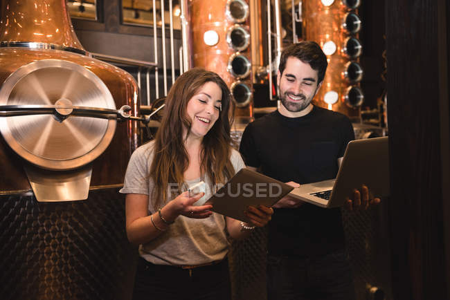 Man and woman using digital tablet and laptop in beer factory — Stock Photo
