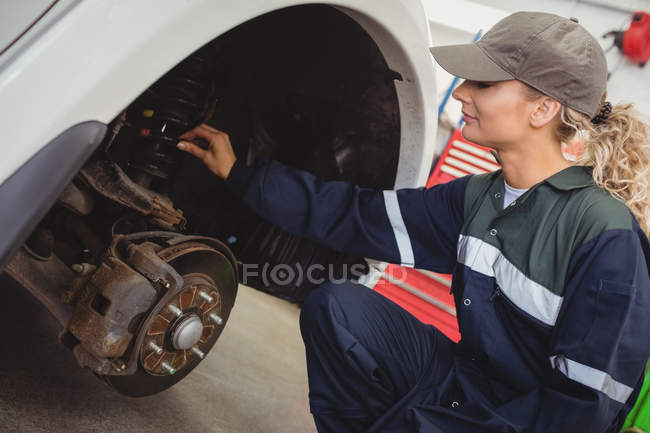 Mecânico feminino examinando um freio de disco de roda de carro na garagem de reparo — Fotografia de Stock