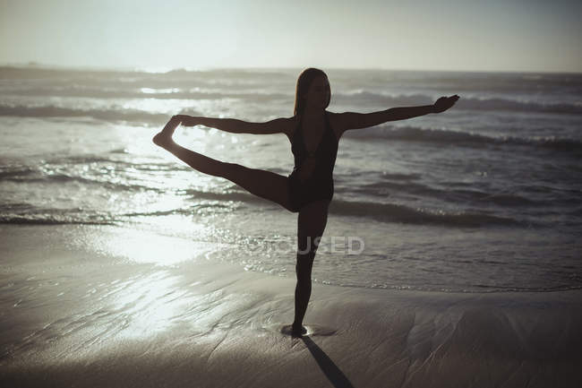 Mulher realizando ioga na praia ao entardecer — Fotografia de Stock