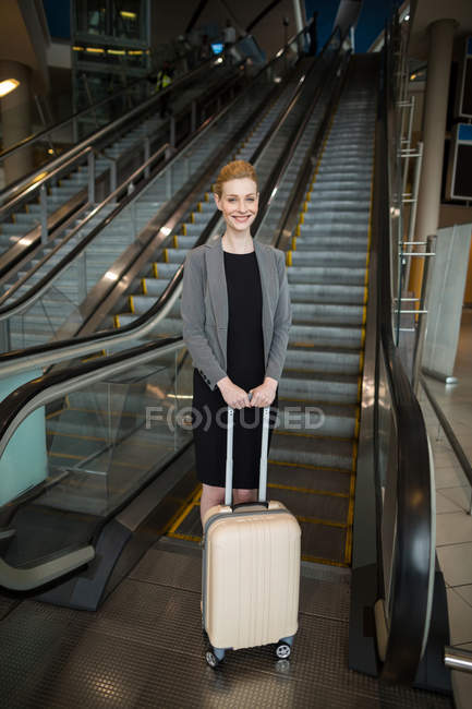 Empresária de pé perto de escada rolante com bagagem no aeroporto — Fotografia de Stock