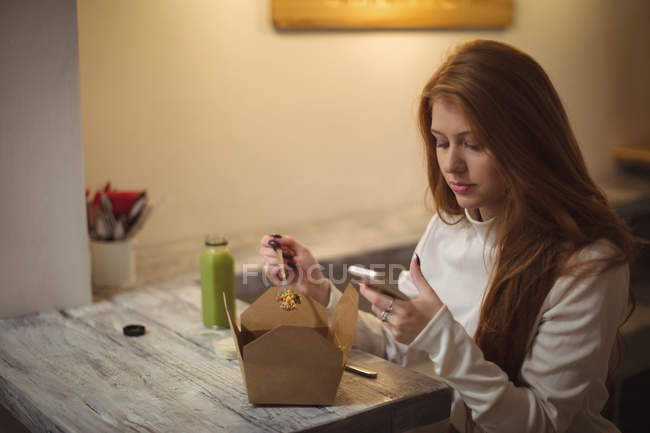 Рыжая женщина использует мобильный телефон во время еды салата — стоковое фото