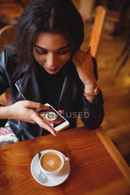 Schöne Frau klickt Foto von Kaffee von Handy in Café — Stockfoto