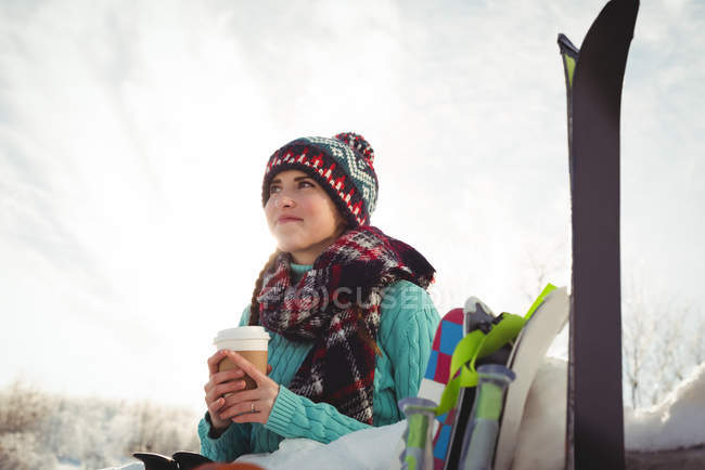 Mujer esquiadora con taza de café mirando hacia arriba y sonriendo en la estación de esquí - foto de stock