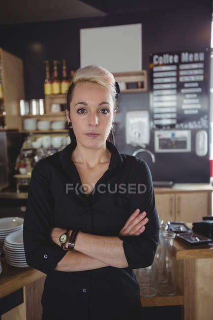 Retrato de camarera de pie con los brazos cruzados en la cafetería - foto de stock