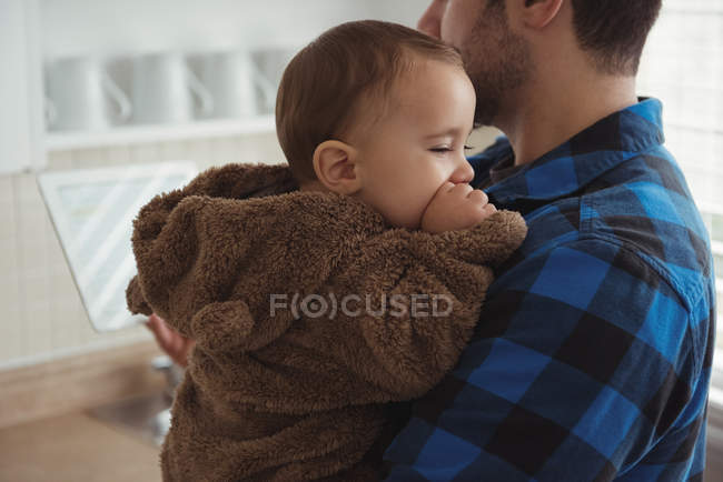 Father holding baby son while standing in kitchen at home — Stock Photo