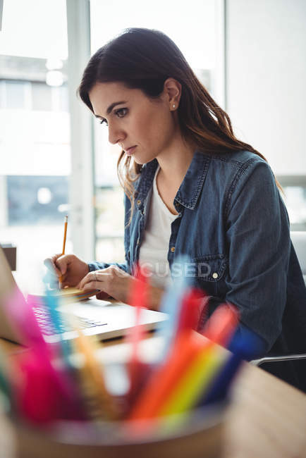 Бизнес-руководитель смотрит на ноутбук и пишет на липких заметках в офисе — стоковое фото