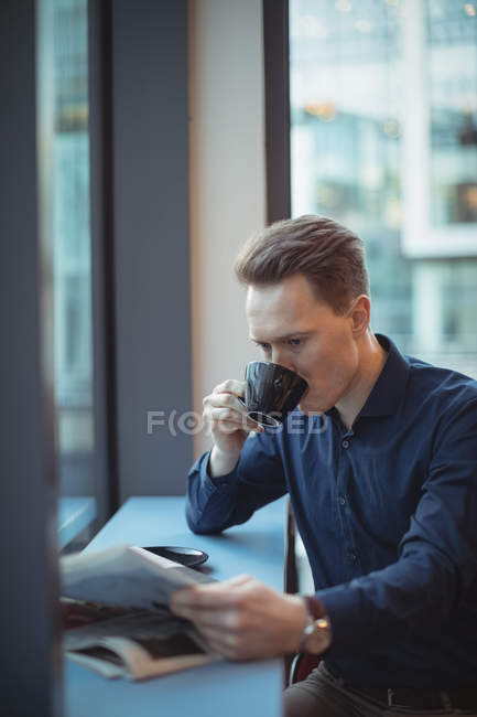 Hombre ejecutivo leyendo el periódico mientras toma café en la cafetería - foto de stock