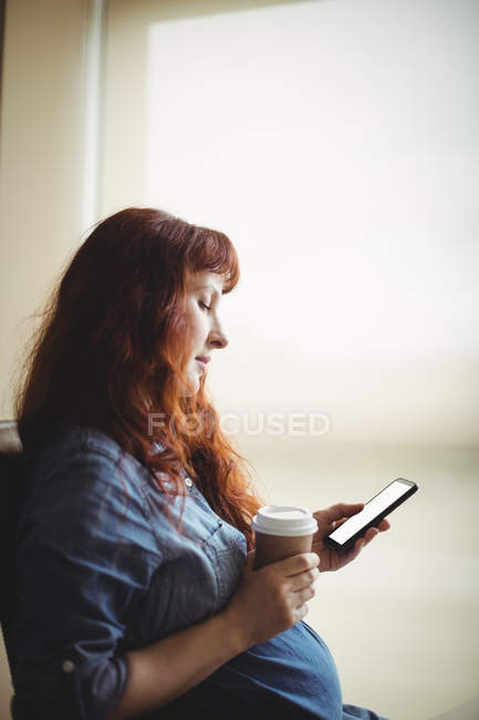 Schwangere Geschäftsfrau nutzt Handy beim Kaffee im Büro — Stockfoto