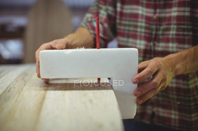 Close-up of man using marking gauge on surfboard in workshop — Stock Photo