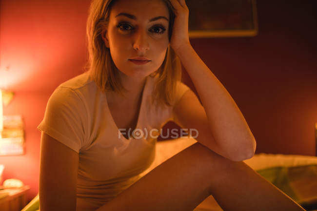 Portrait de femme réfléchie assise sur le lit dans la chambre — Photo de stock