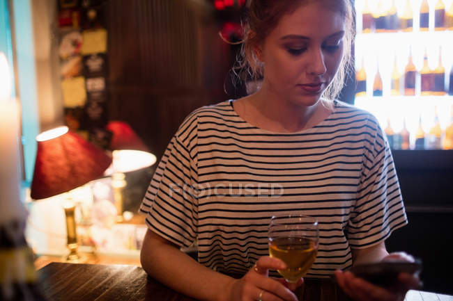 Schöne Frau benutzt Handy, während sie Wein in der Bar trinkt — Stockfoto