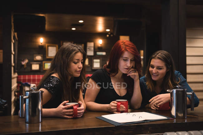 Amigos sosteniendo tazas de café y mirando el menú en el mostrador del bar - foto de stock