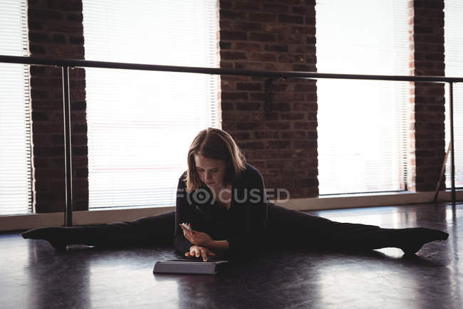 Танцовщица сидит на полу, растягивает и использует цифровой планшет в танцевальной студии — стоковое фото