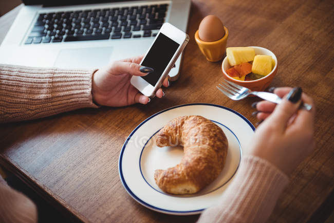 Frau benutzt Handy beim Frühstück im heimischen Wohnzimmer — Stockfoto