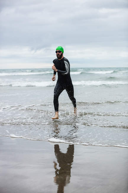 Спортсмен у вологому костюмі, що бігає на пляжі — стокове фото