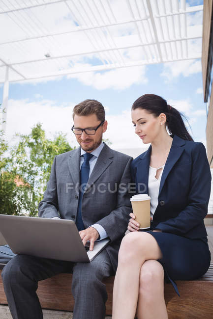 Бизнесмен и коллега сидят снаружи офисного здания и пользуются ноутбуком — стоковое фото
