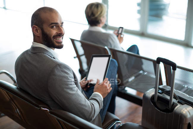 Портрет усміхненого бізнесмена, який використовує цифровий планшет у зоні очікування в терміналі аеропорту — стокове фото