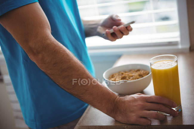 Середній розділ чоловіка, який використовує свій мобільний телефон, тримаючи вдома склянку соку — стокове фото