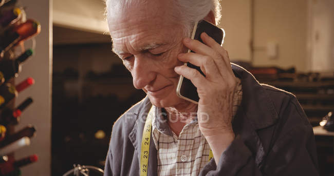 Чоботар говорити на мобільний телефон у майстерні — стокове фото